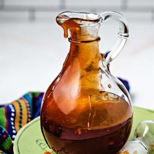 honey sriracha sauce in a glass decanter sitting on a green plate.