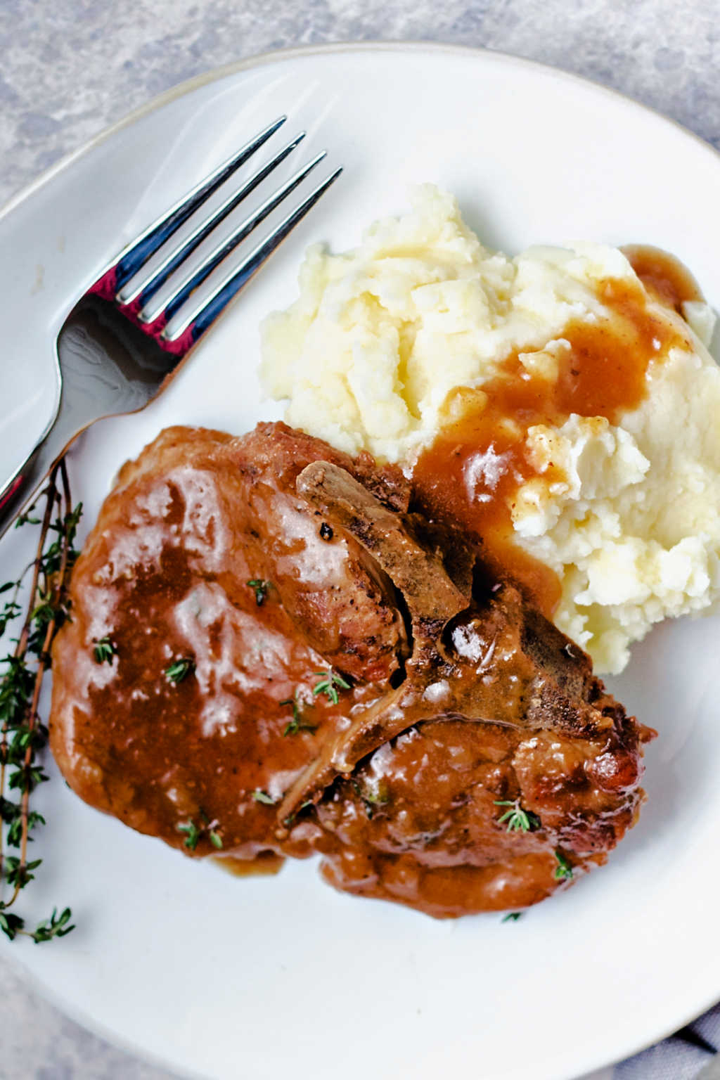 instant pot pork chop with apple gravy over mashed potatoes on a white plate.