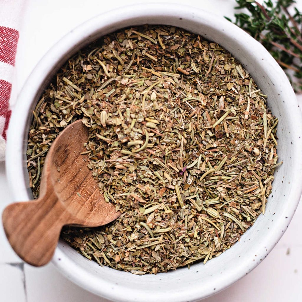 italian seasoning substitute in a white bowl with a wooden spoon on a table.