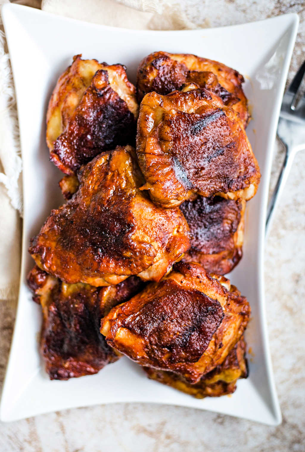 smoked chicken thighs on a white platter on a table with a meat fork.