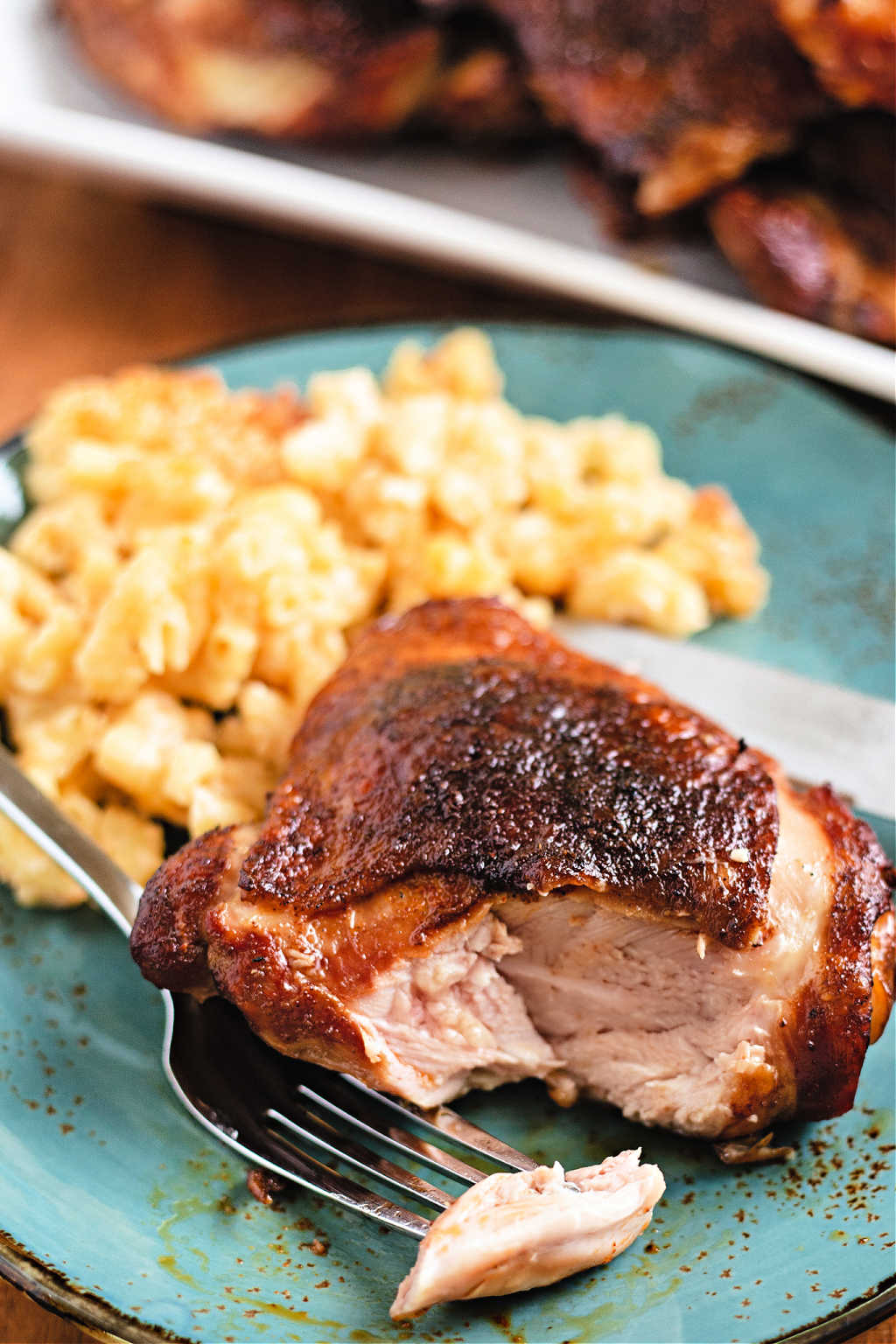 smoked chicken thigh on a blue plate with mac and cheese.