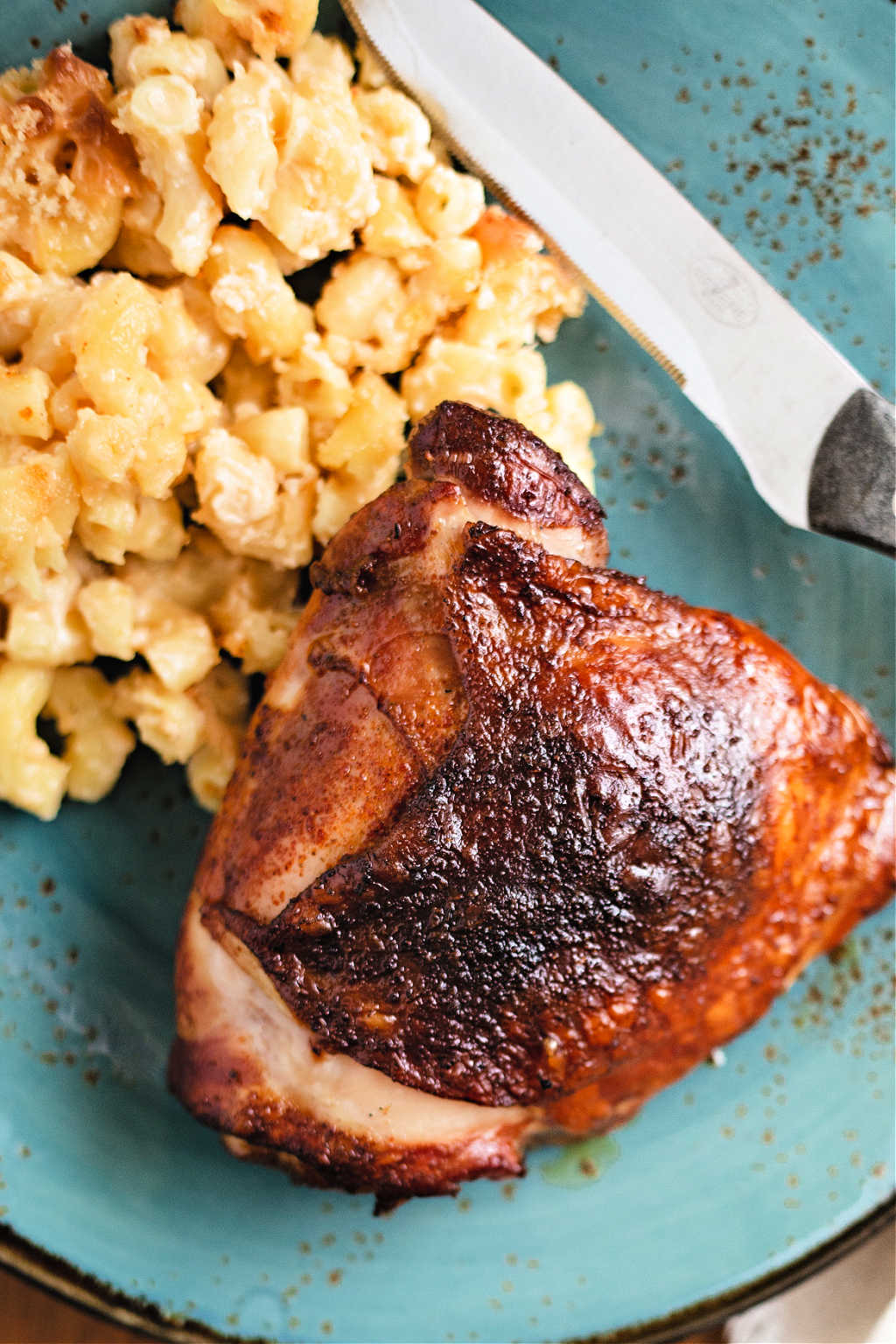 smoked chicken thigh on a blue plate with mac and cheese.