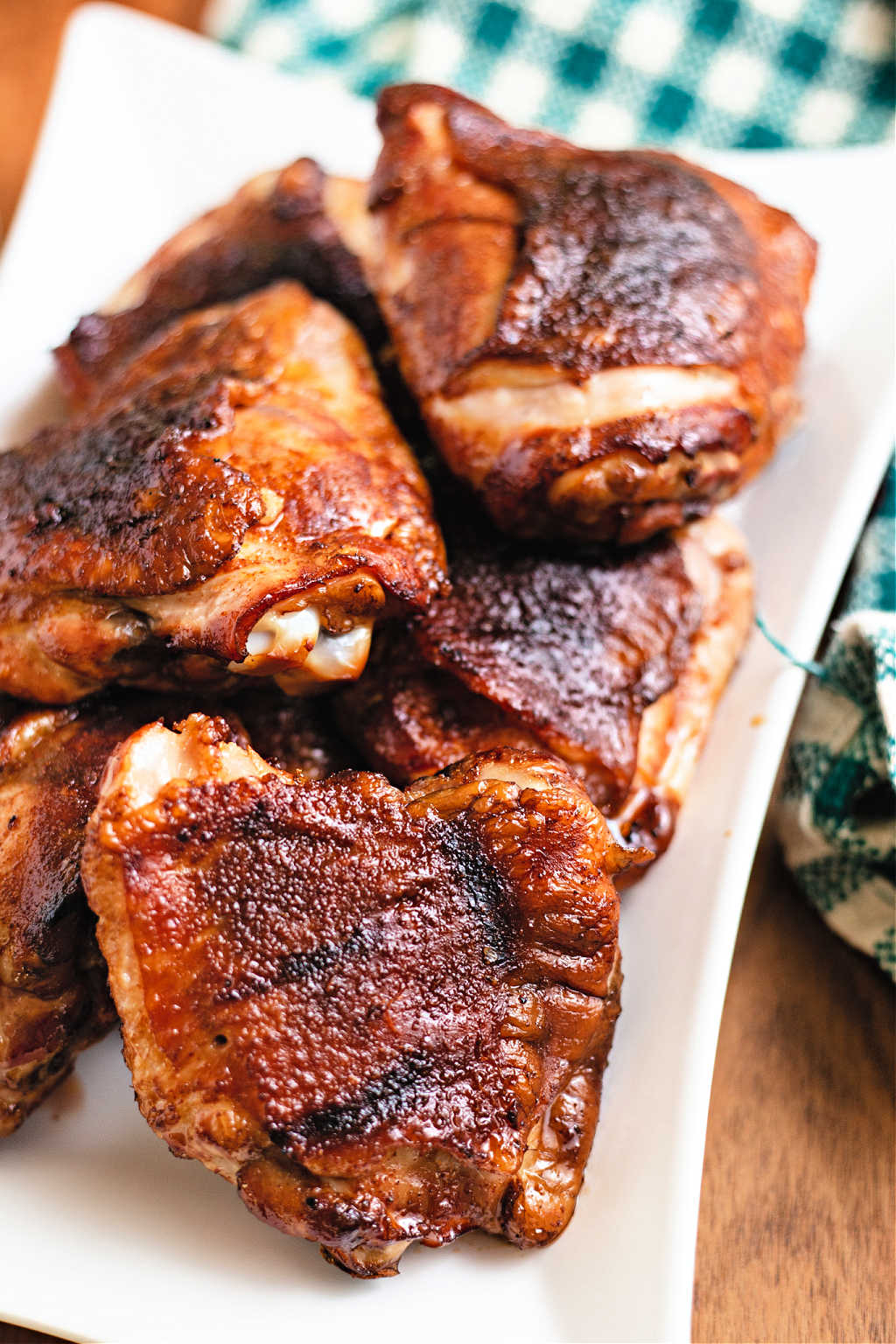 smoked chicken thighs on a white platter on a table with a meat fork.