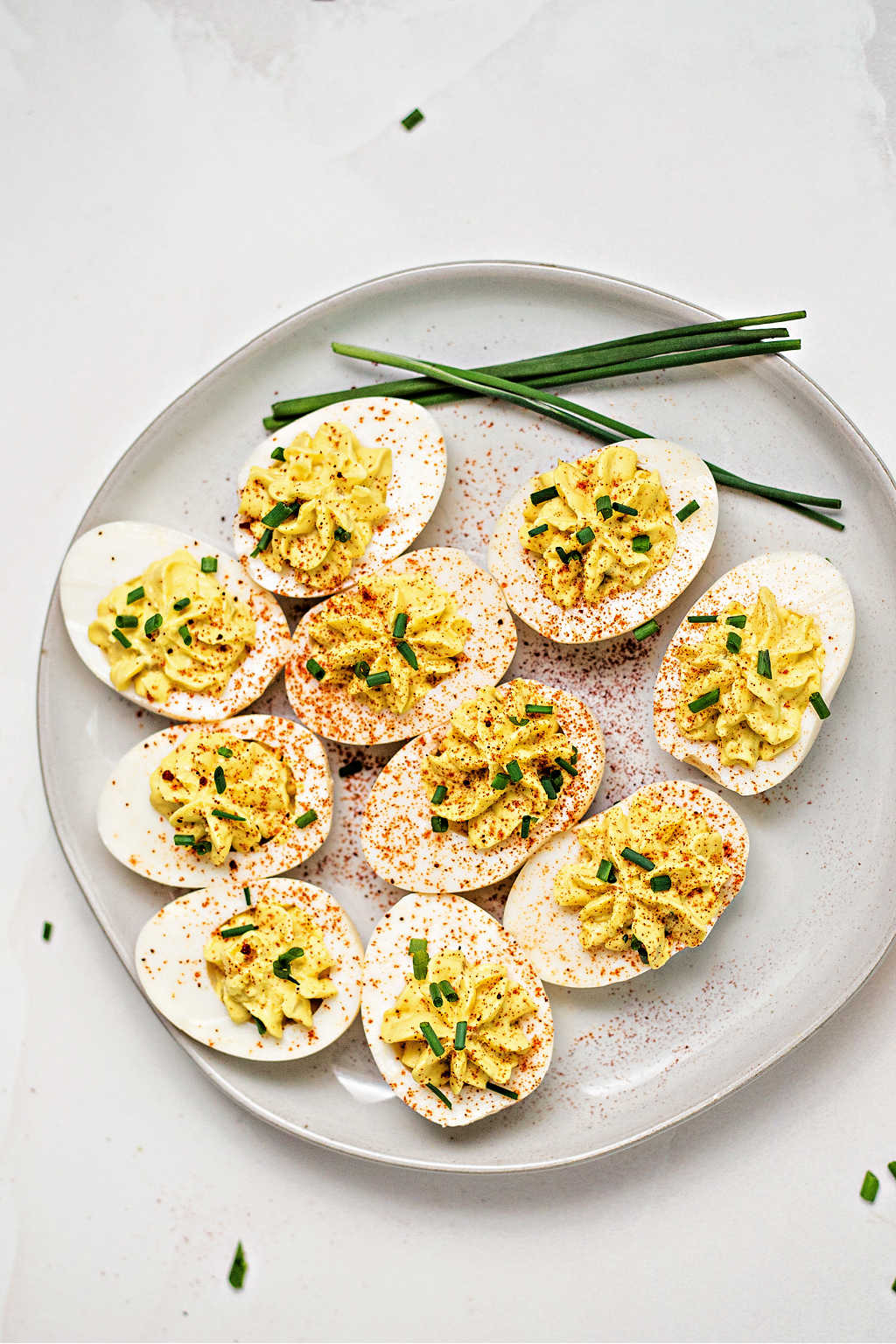 a plate of southern deviled eggs on a table garnished with paprika and chives.