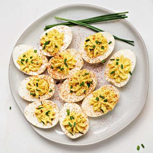 a plate of southern deviled eggs on a table garnished with paprika and chives.