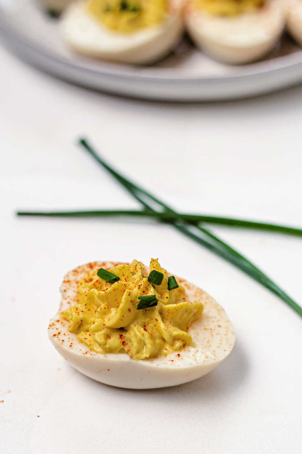 a single southern deviled egg on a table garnished with paprika and chives.