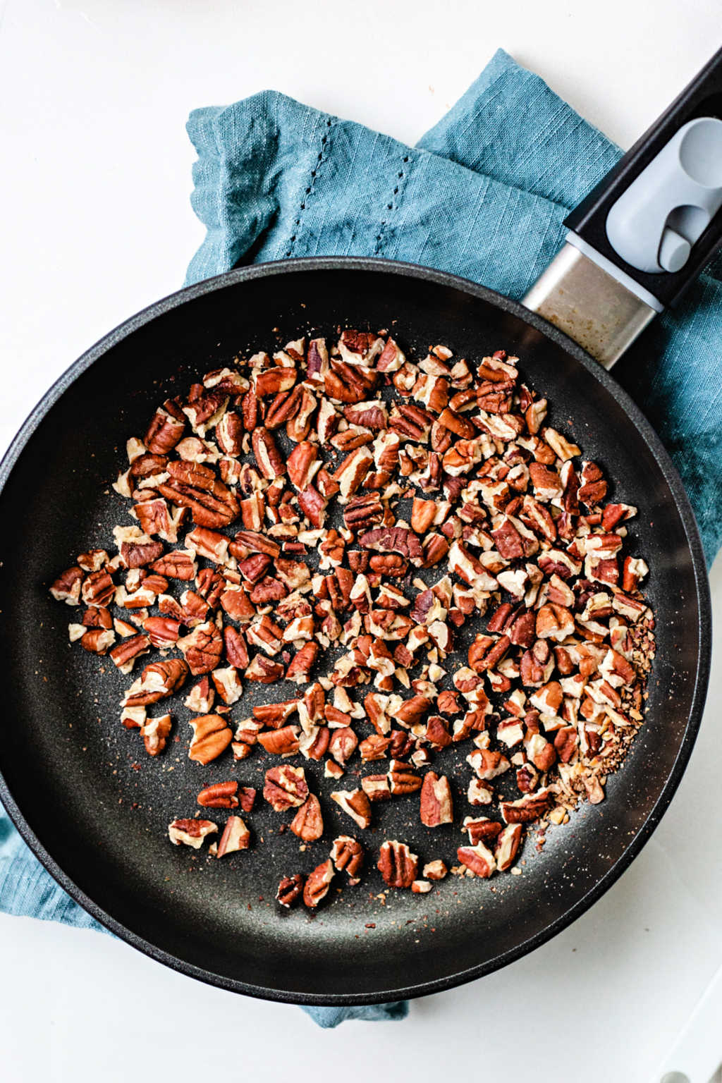 toasted pecans in a non stick skillet on a counter.