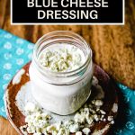 buttermilk blue cheese dressing in a mason jar with blue cheese crumbles on top sitting on a wooden table.