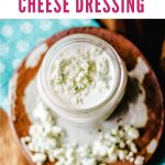 buttermilk blue cheese dressing in a mason jar with blue cheese crumbles on top sitting on a wooden table.