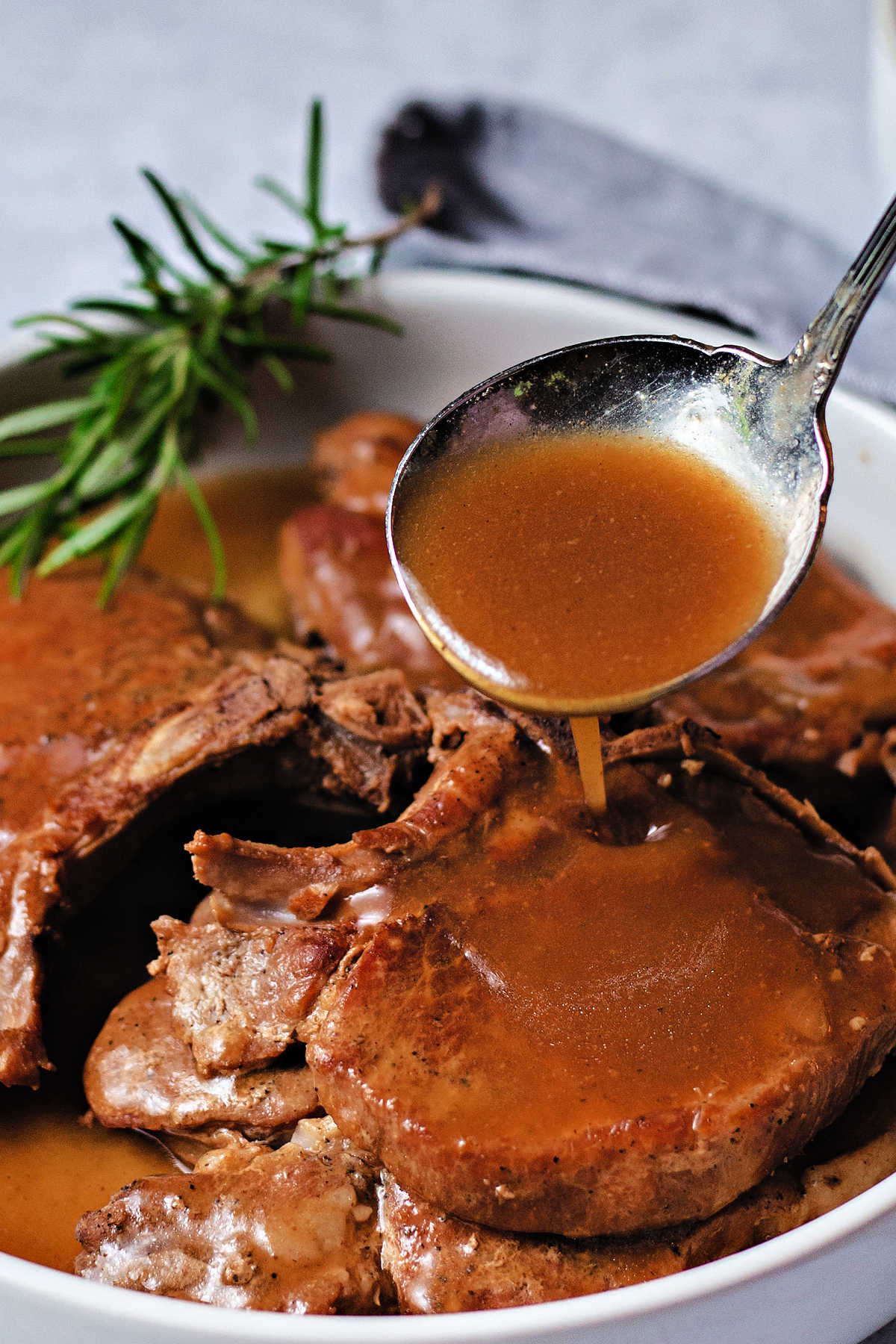 spooning gravy over instant pot pork chops in a white serving dish.