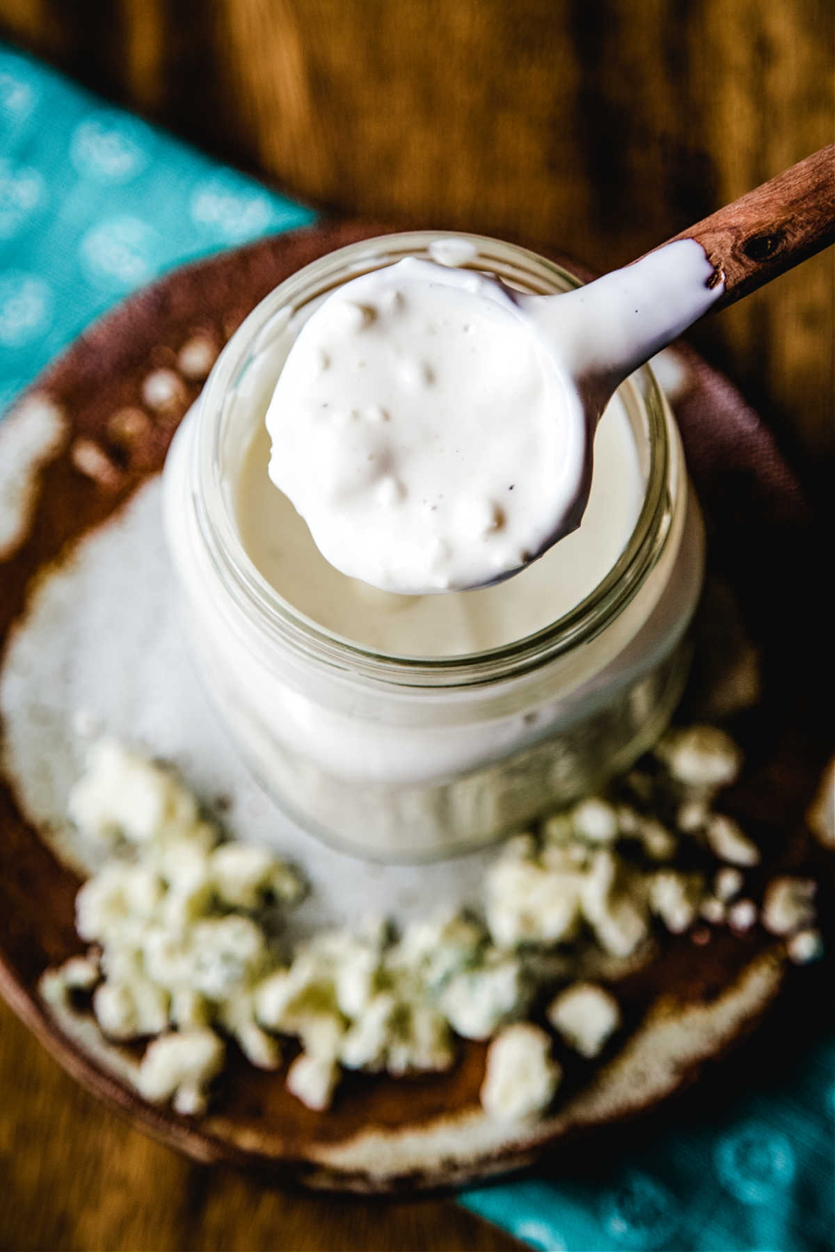 a wooden spoon in a jar of buttermilk blue cheese dressing sitting on a wooden table.