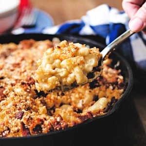 a spoonful of smoked mac and cheese being lifted out of a cast iron skillet.