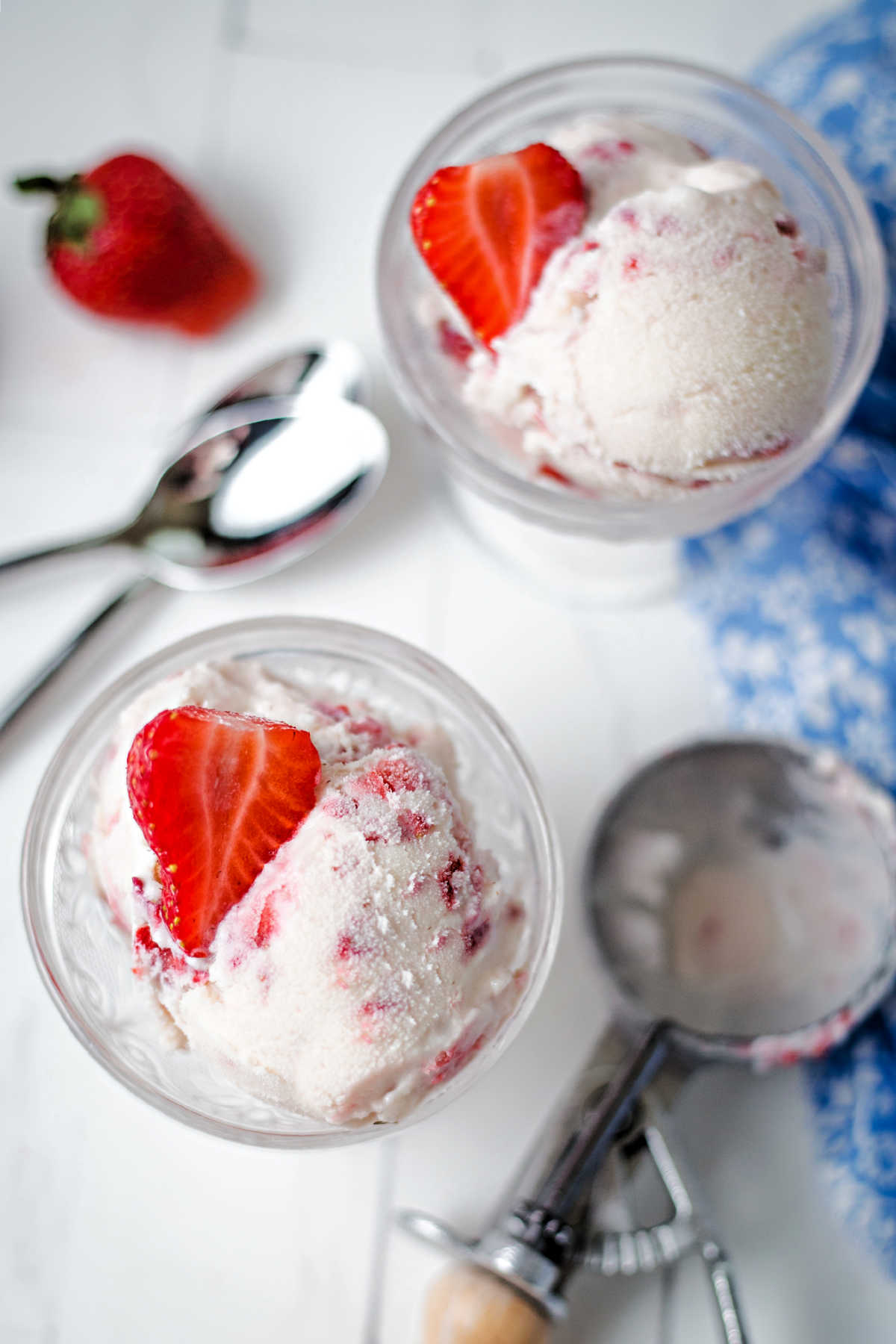 two ice cream bowls with scoops of homemade strawberry ice cream with an ice cream scoop laying on the table.