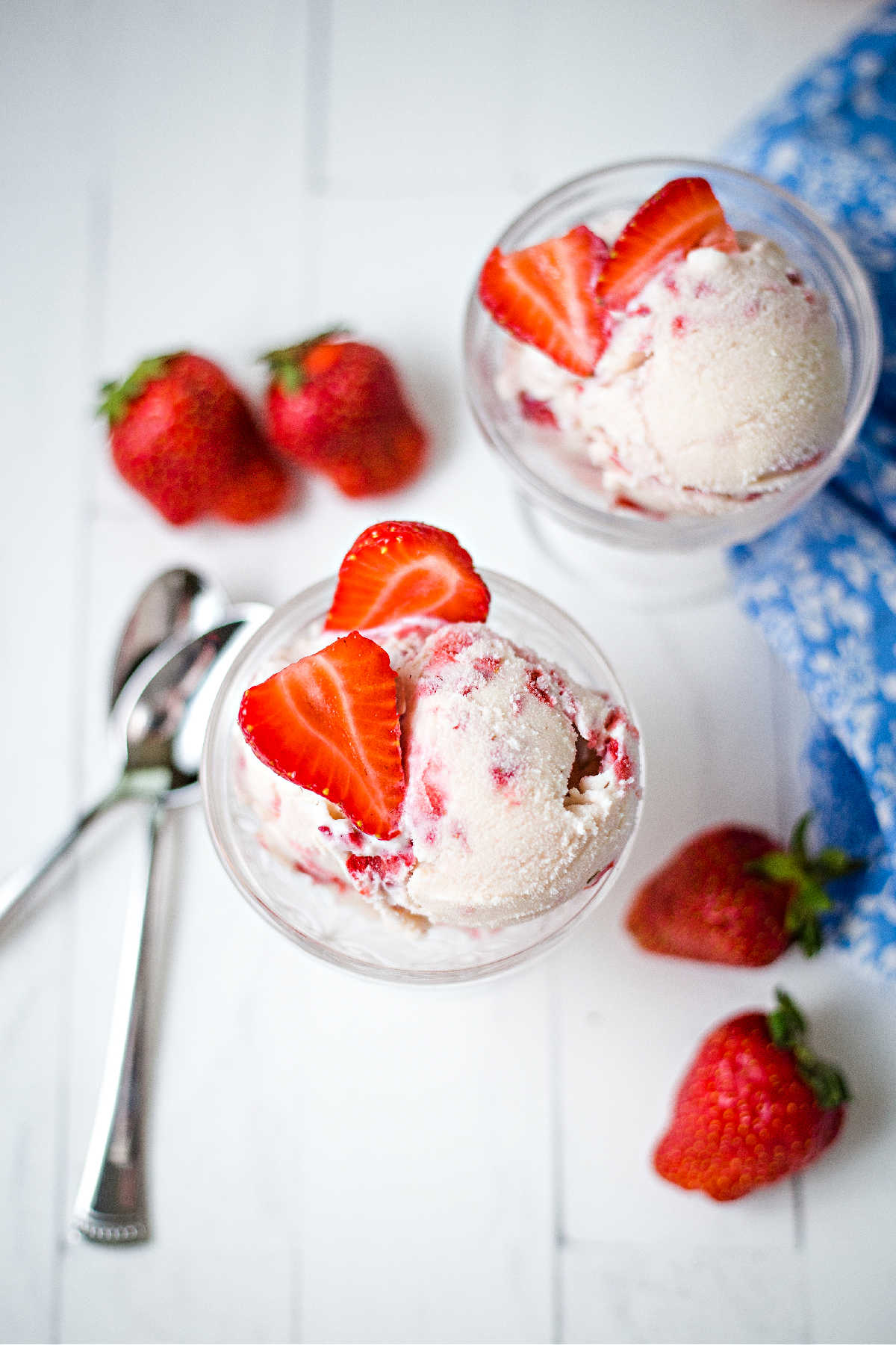 two ice cream bowls with scoops of homemade strawberry ice cream on a table with two spoons.