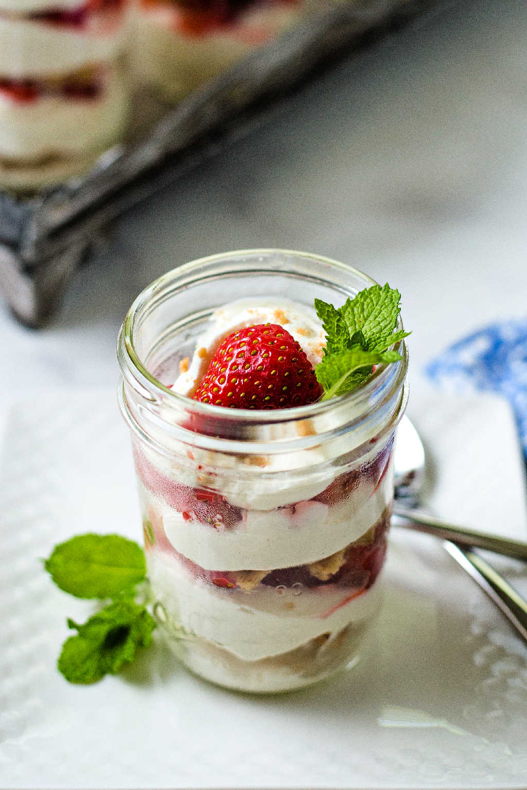 strawberry icebox cake in a mason jar on a white plate with a spoon and sprig of mint.