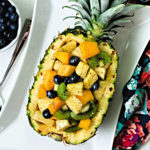 a hollowed out pineapple with tropical fruit salad on a white platter.