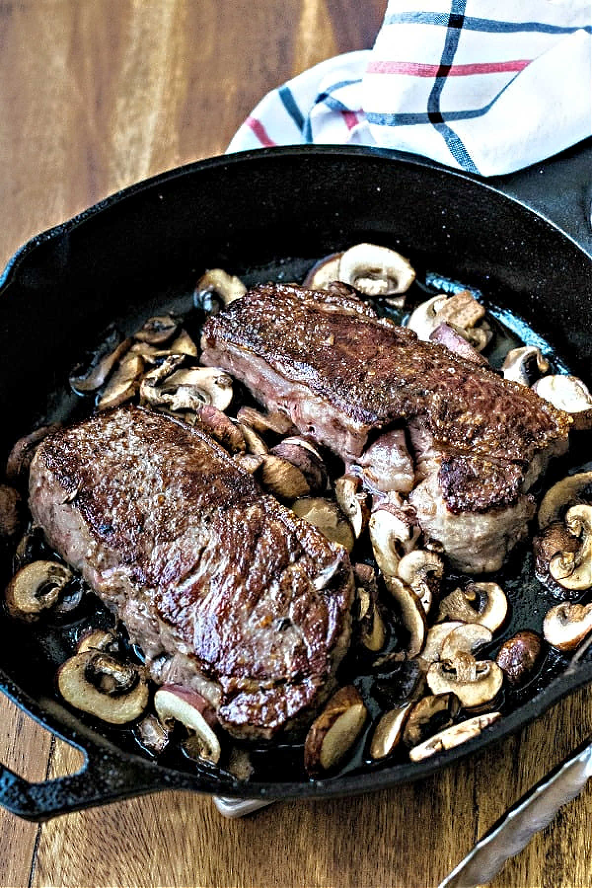 two new york strip steaks in a cast iron skillet on a wooden table.
