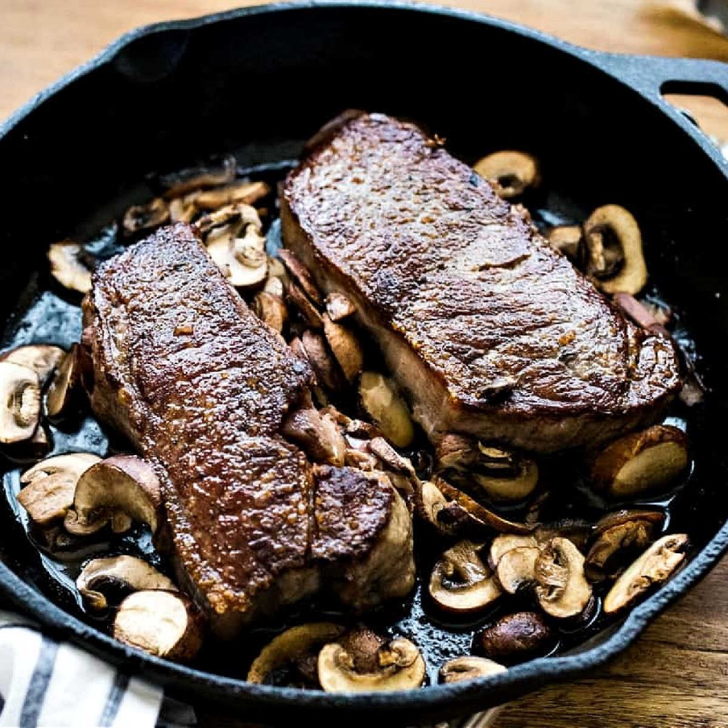 two new york strip steaks in a cast iron skillet on a wooden table.
