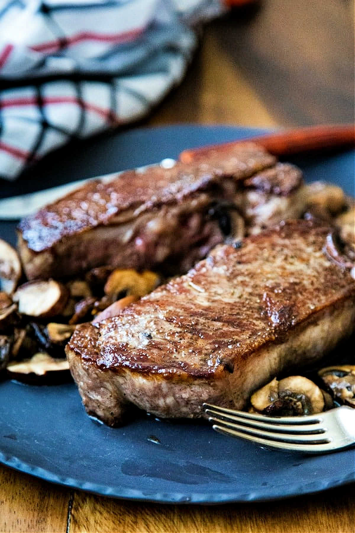 a pan-seared new york strip on a slate plate with sauteed mushrooms on a wooden table.