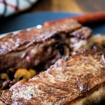 two New York strip steaks with mushrooms on a slate plate.