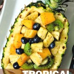 TROPICAL FRUIT SALAD IN A PINEAPPLE BOWL ON A WHITE PLATE.