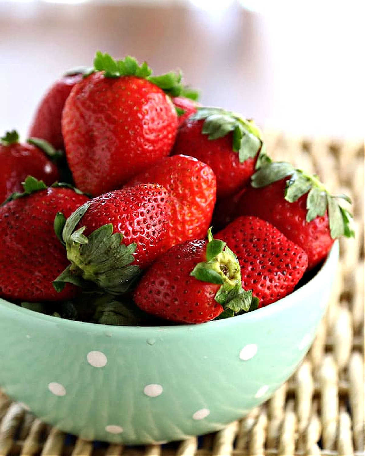 a green and white polka dot bowl filled with fresh strawberries.