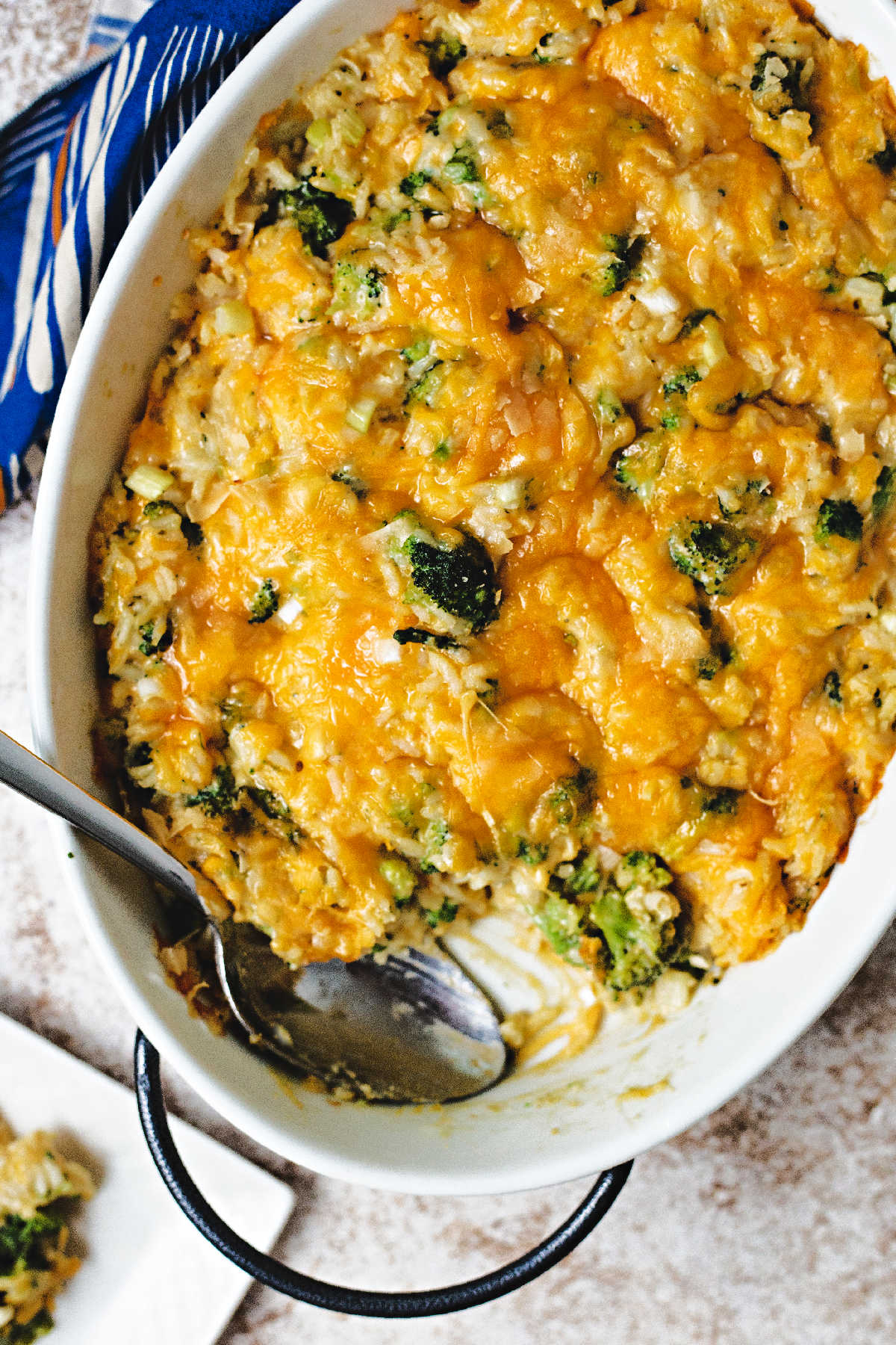 cheesy broccoli rice casserole in a white oval dish with a spoon on a table.