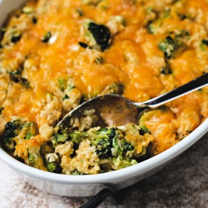 cheesy broccoli rice casserole in a white oval dish with a spoon on a table.