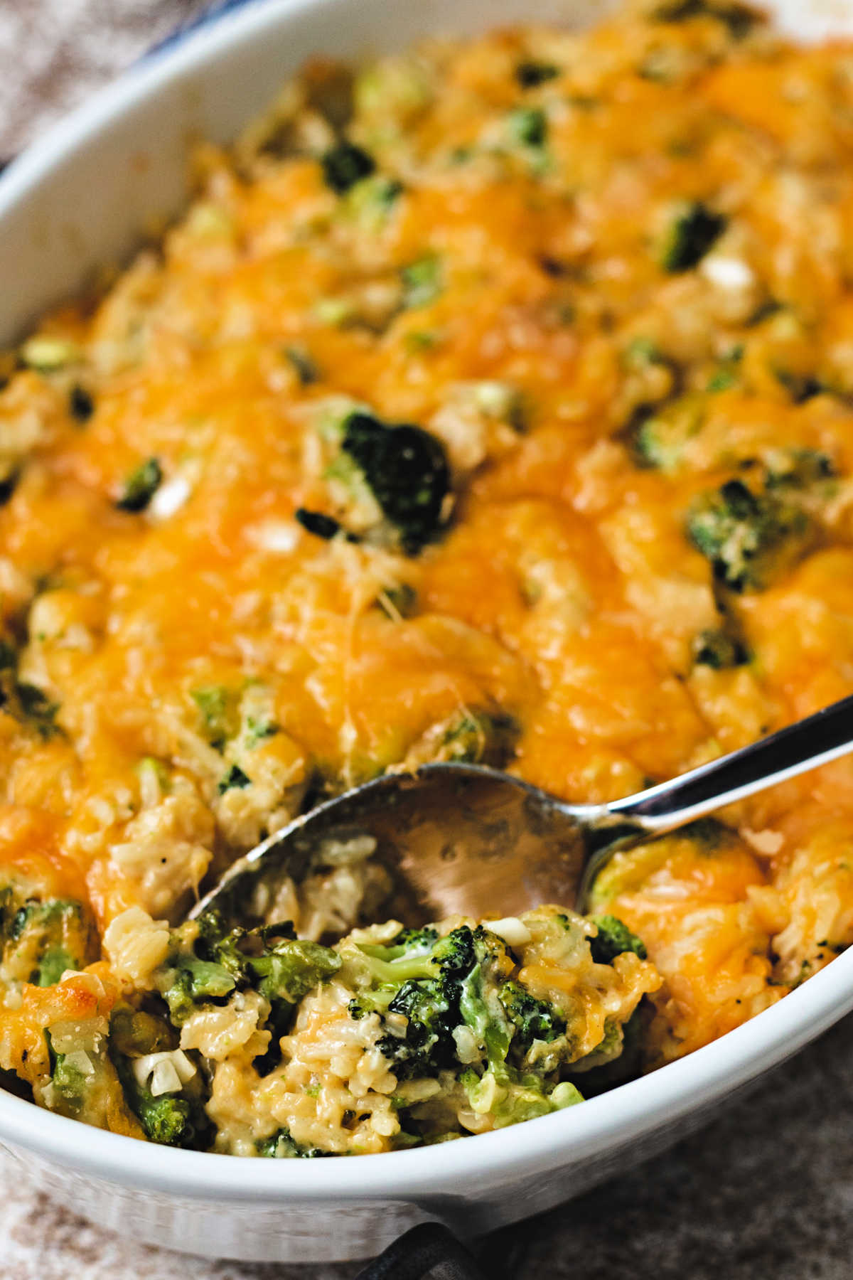 cheesy broccoli rice casserole in a white oval dish with a spoon on a table.