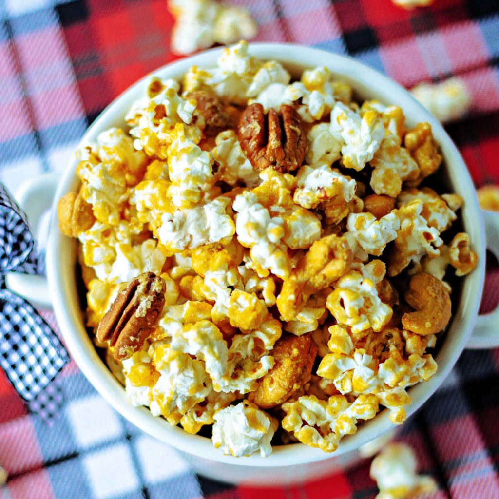 caramel corn with nuts in a bowl sitting on a plaid table cloth.