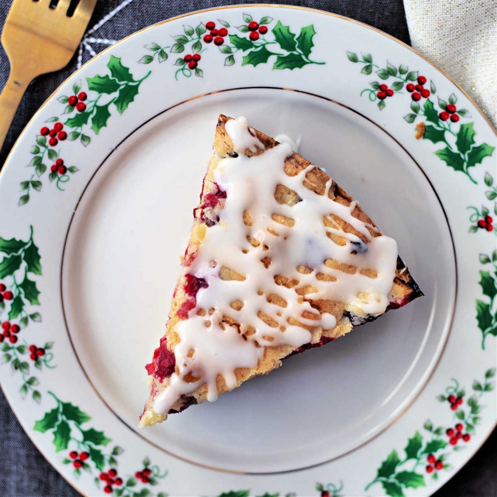 a slice of christmas cranberry cake on a china plate adorned with holly.