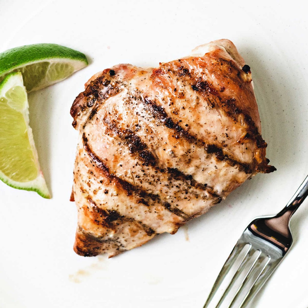 grilled chicken breast on a white plate with lime wedges and a fork.