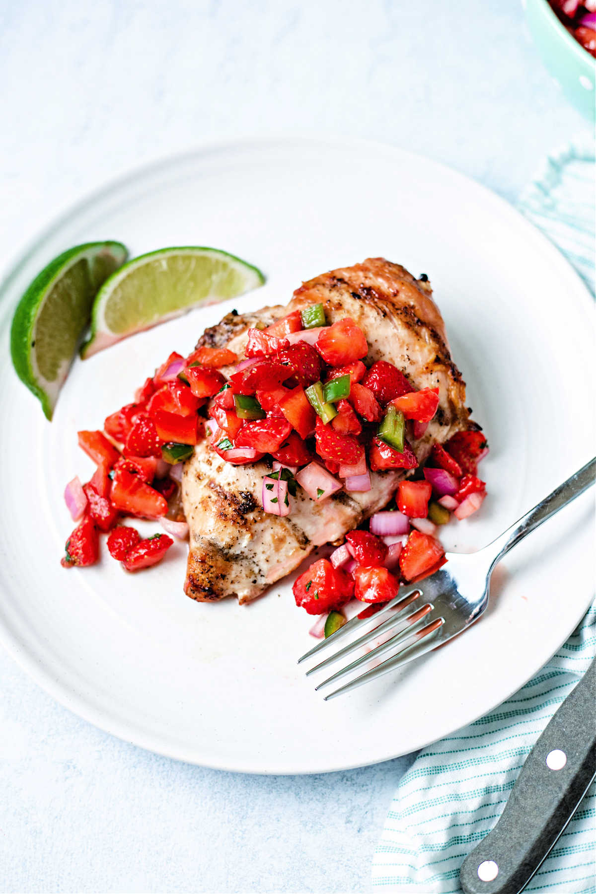a grilled chicken breast with strawberry salsa spooned over top on a white plate.