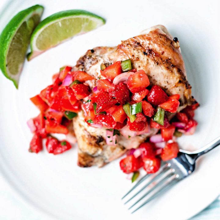 a grilled chicken breast with strawberry salsa spooned over top on a white plate.