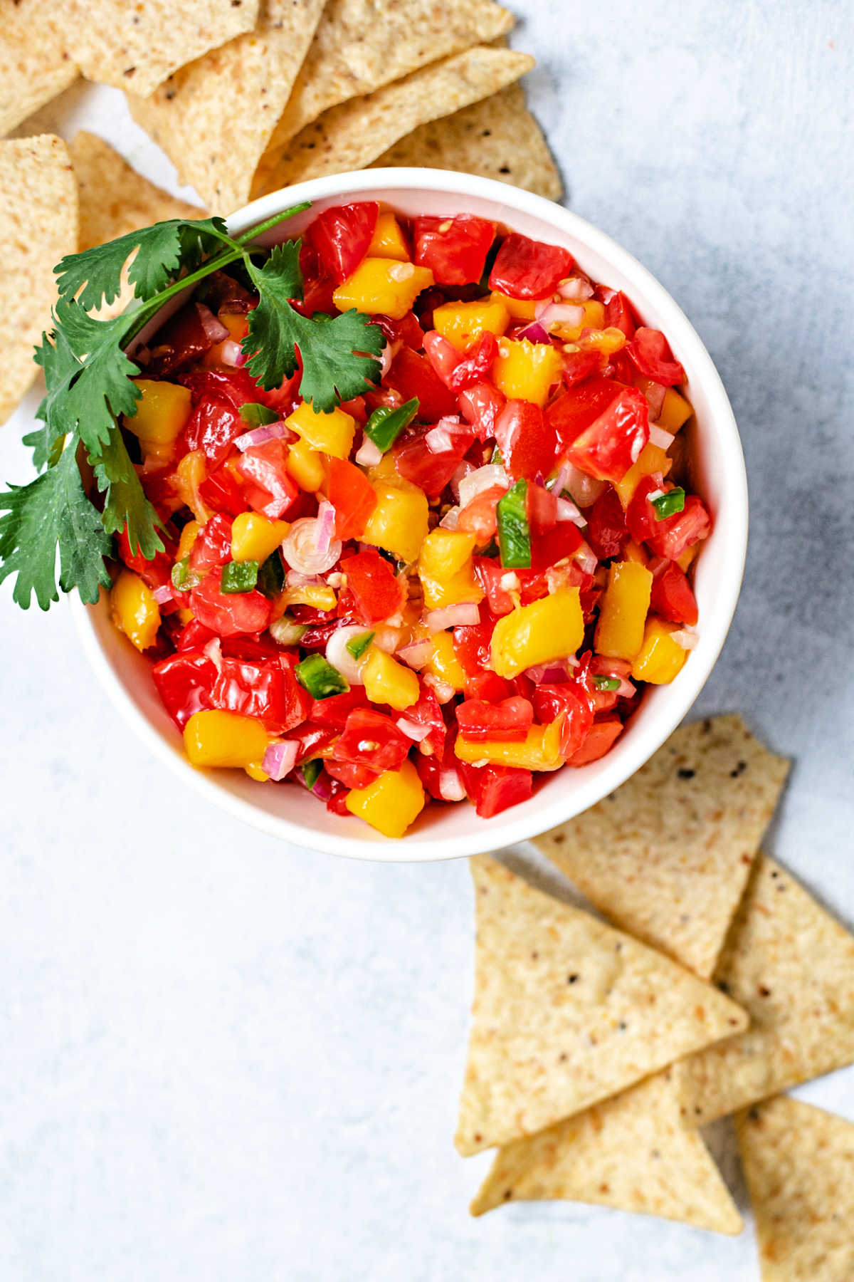 a bowl of mango tomato salsa on a table with tortilla chips scattered around.