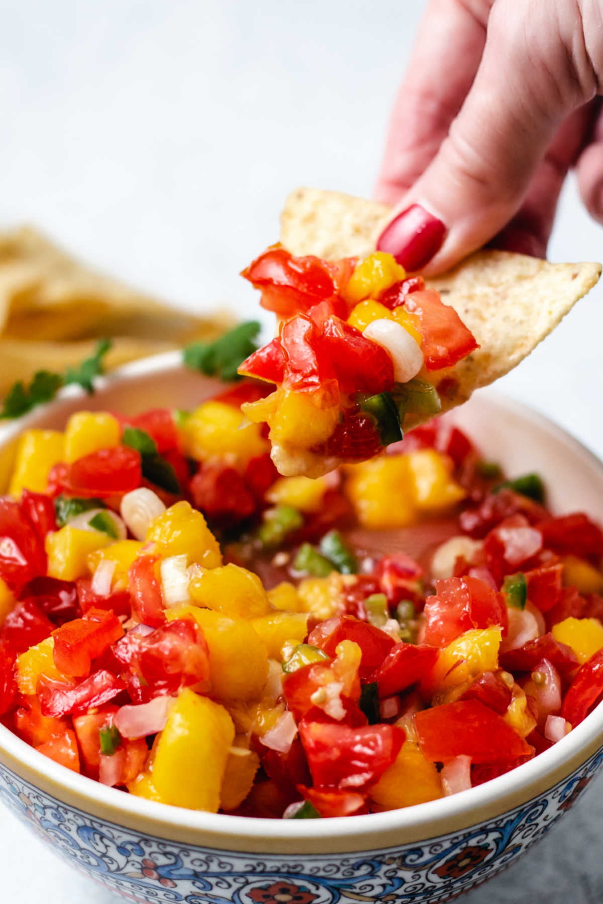 dipping a tortilla chip into a bowl of mango tomato salsa.