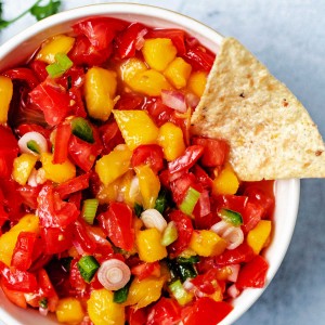 mango tomato salsa in a bowl with a tortilla chip dipping into the bowl.