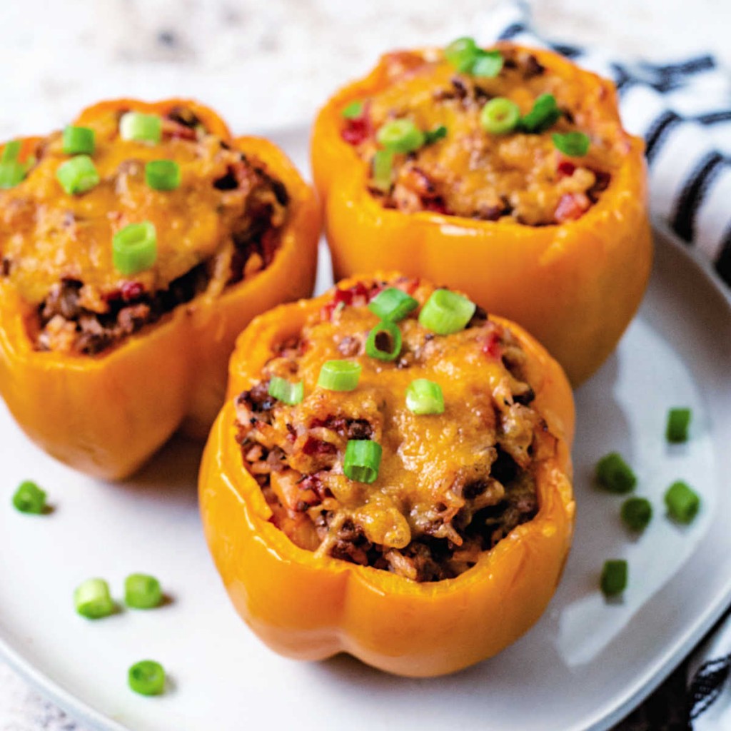 3 air fryer stuffed peppers with melted cheese on a plate garnished with chopped green onions.
