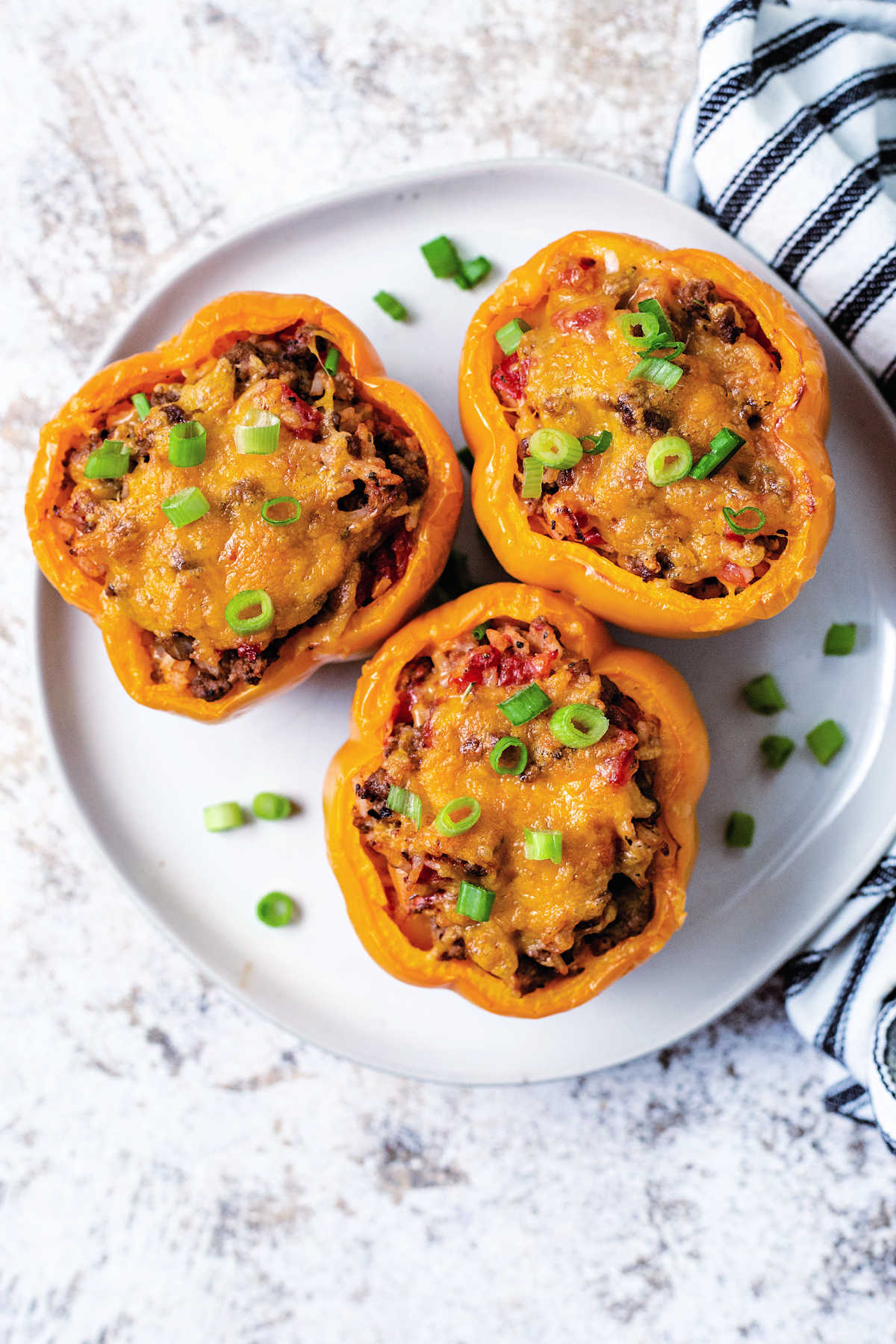 top down view of 3 air fryer stuffed peppers with melted cheese on a plate garnished with chopped green onions.