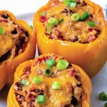 air fryer stuffed peppers with melted cheese on a plate garnished with chopped green onions.