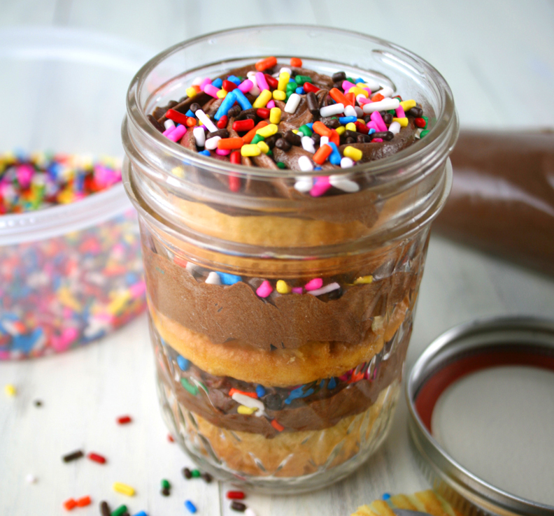 Frosted Chocolate Cupcakes in a mason jar on a table with sprinkles.