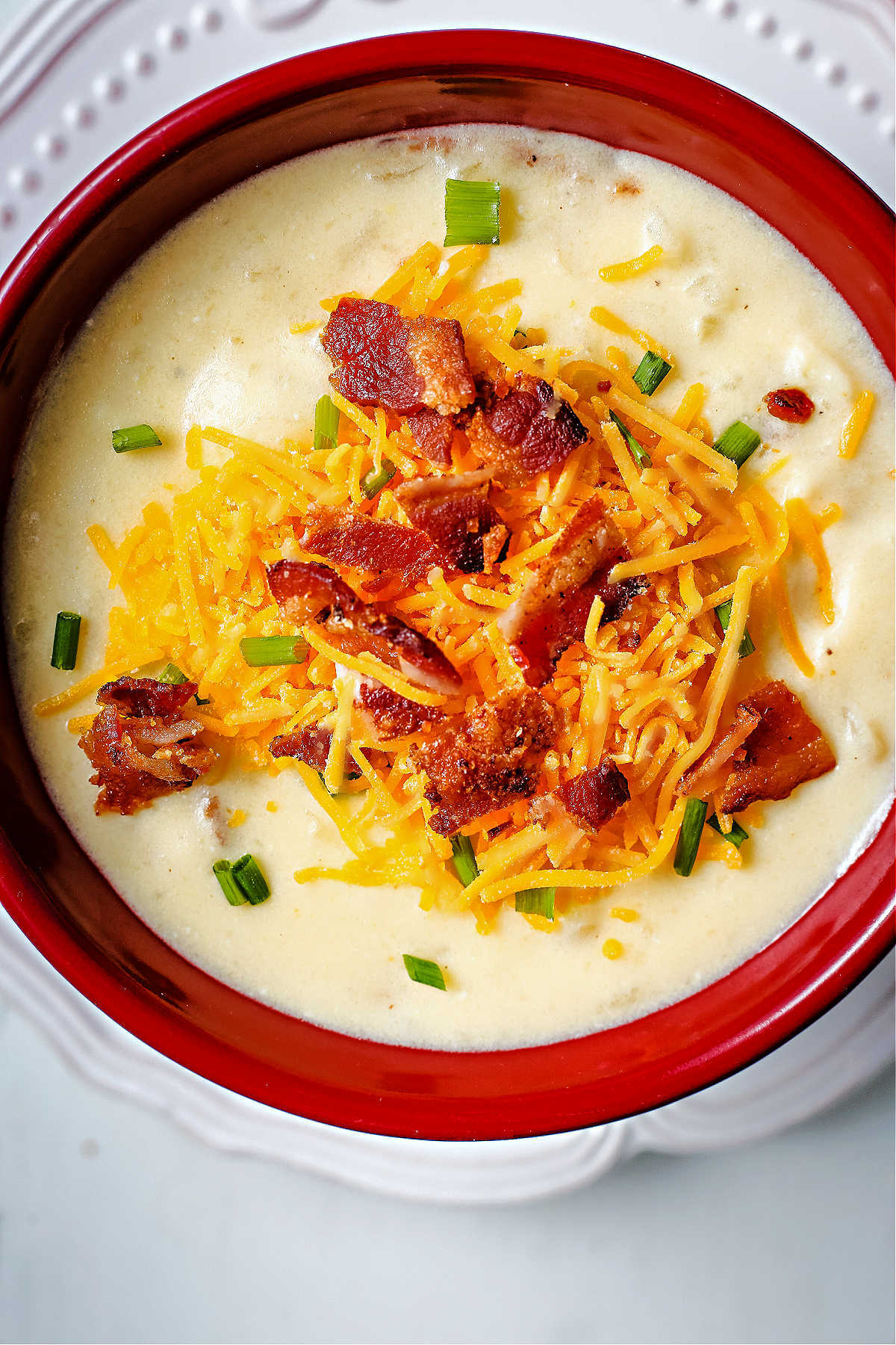 loaded potato soup in a red soup bowl garnished with cheese, bacon, and chives.
