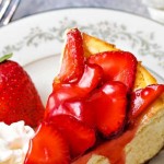 a slice of strawberry cheesecake on a china plate with whipped cream and a strawberry garnish.