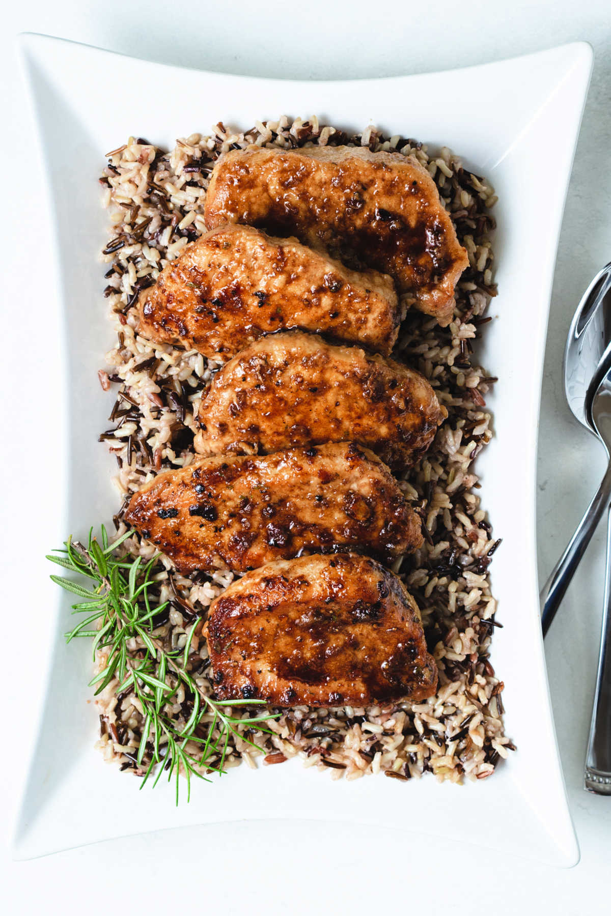 a platter of balsamic pork chops laying on a bed of wild rice on a table.