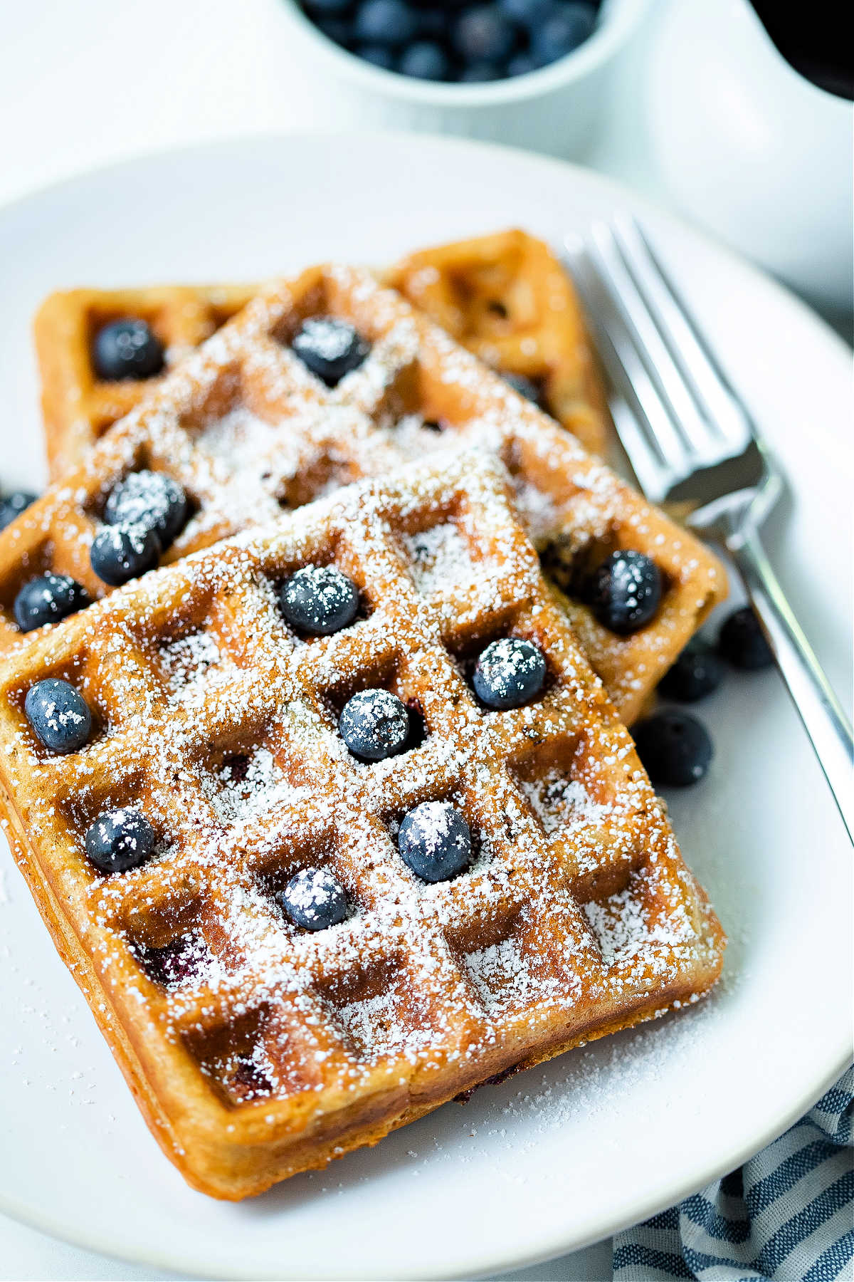 three blueberry waffles on a white plate with a fork to the side.