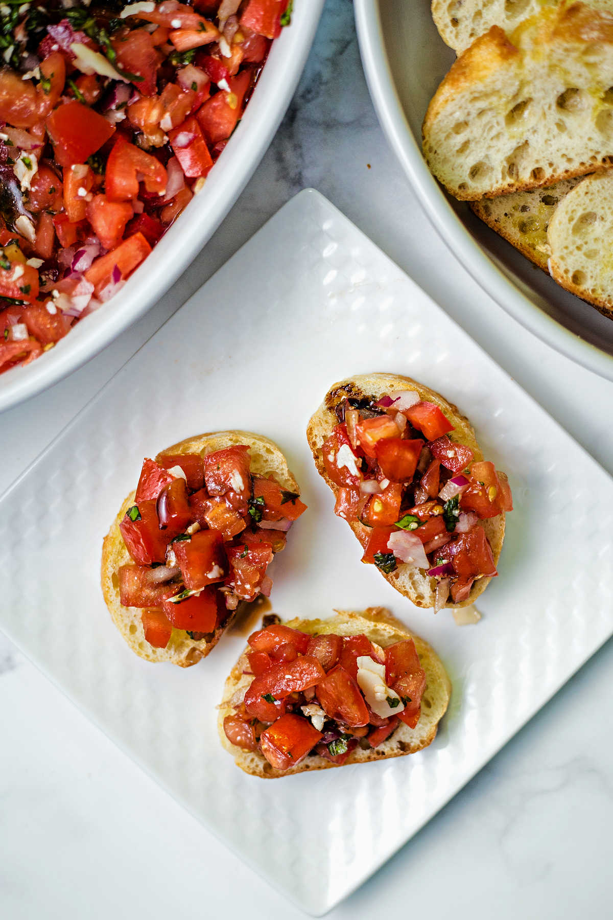 three slices of baguette on a plate with bruschetta piled on top of each one.