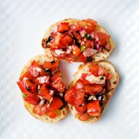 three slices of baguette on a plate with bruschetta piled on top of each one.