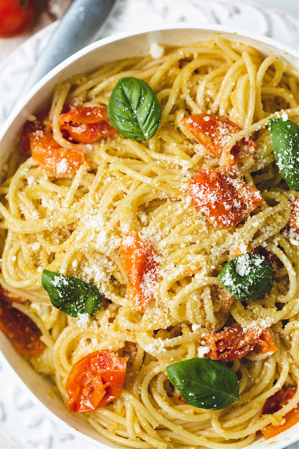 a bowl of cherry tomato pasta garnished with grated parmesan cheese and fresh basil leaves.