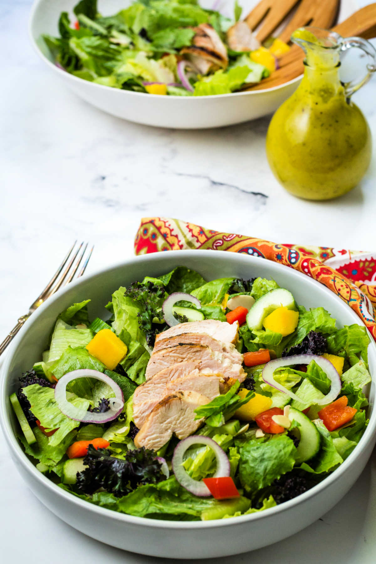 grilled chicken salad in a bowl on a table with a bottle of mango dressing.