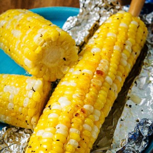 an ear of corn grilled in foil on a plate.